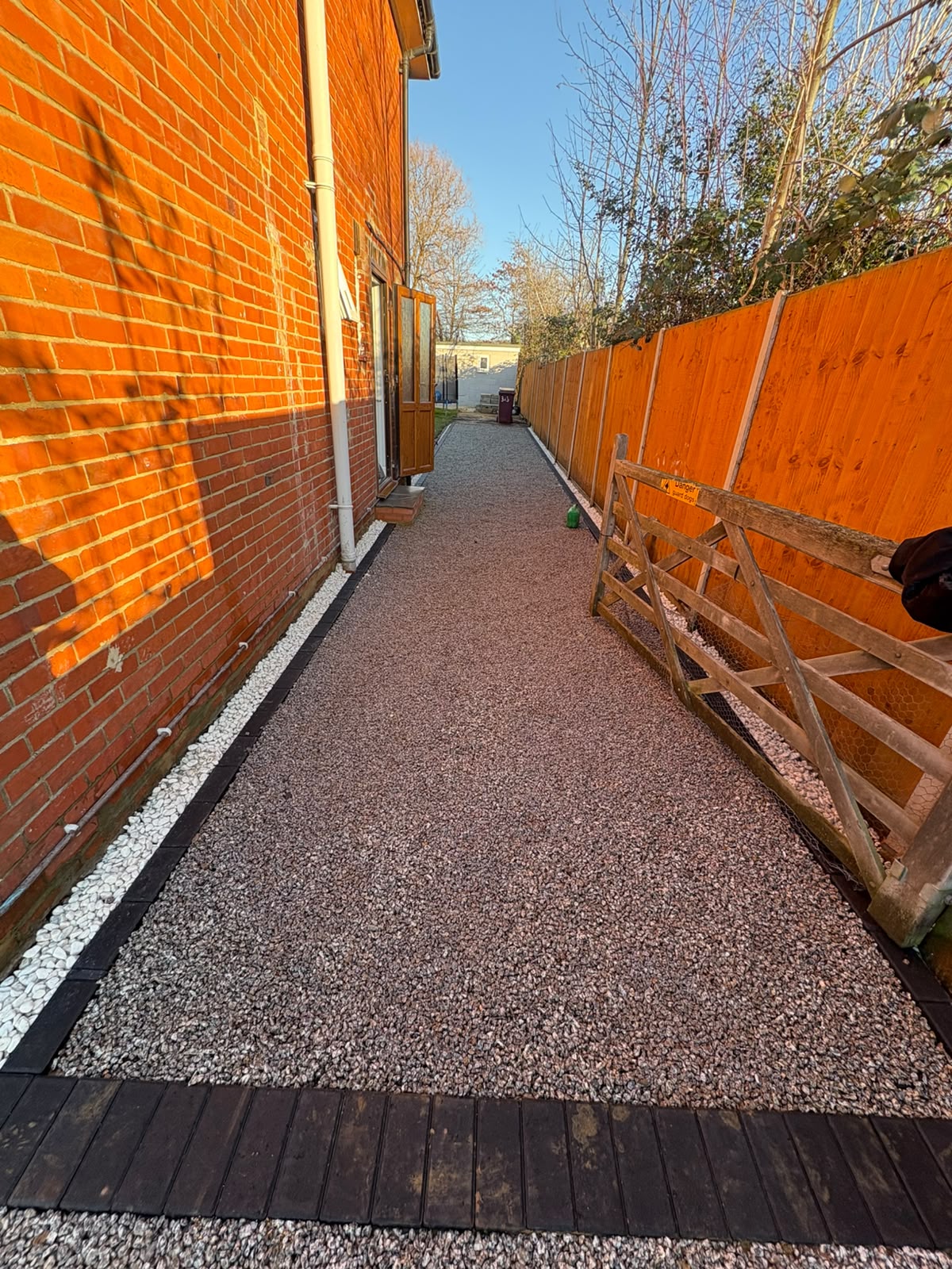 Deep red resin bound side path with block edging beside a house