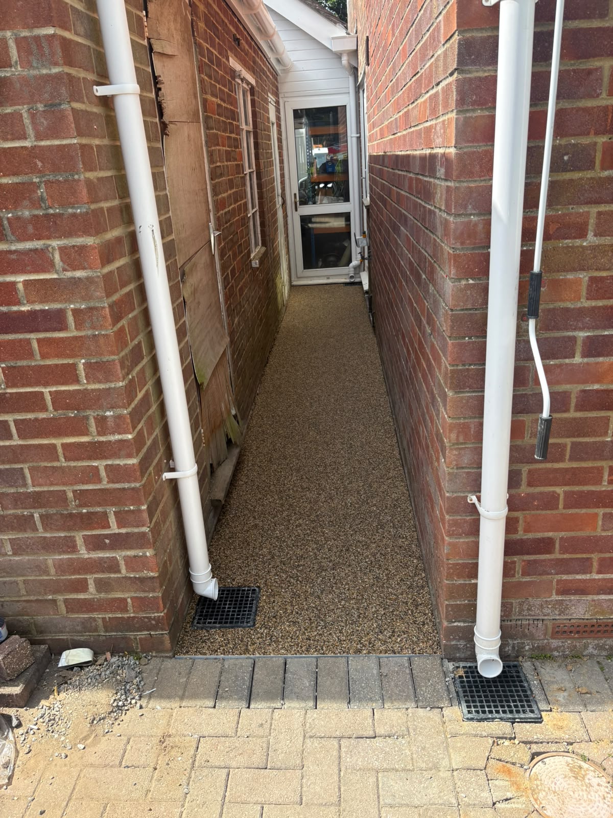 Narrow resin bound pathway between houses with drainage grates installed