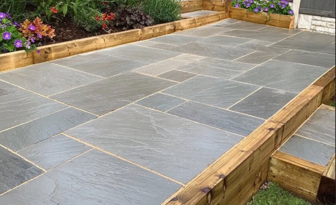 Grey Indian sandstone patio with sleeper retaining edge and planted border