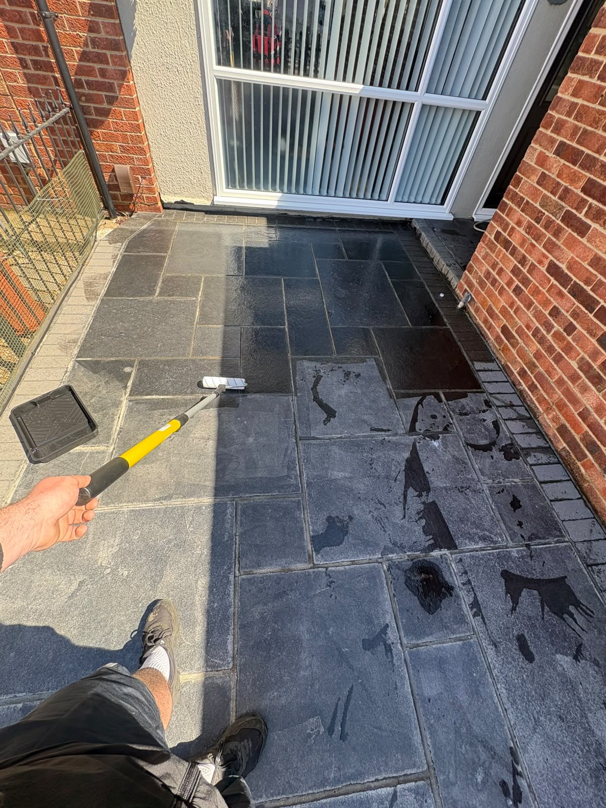 Black limestone patio being sealed with a roller in daylight
