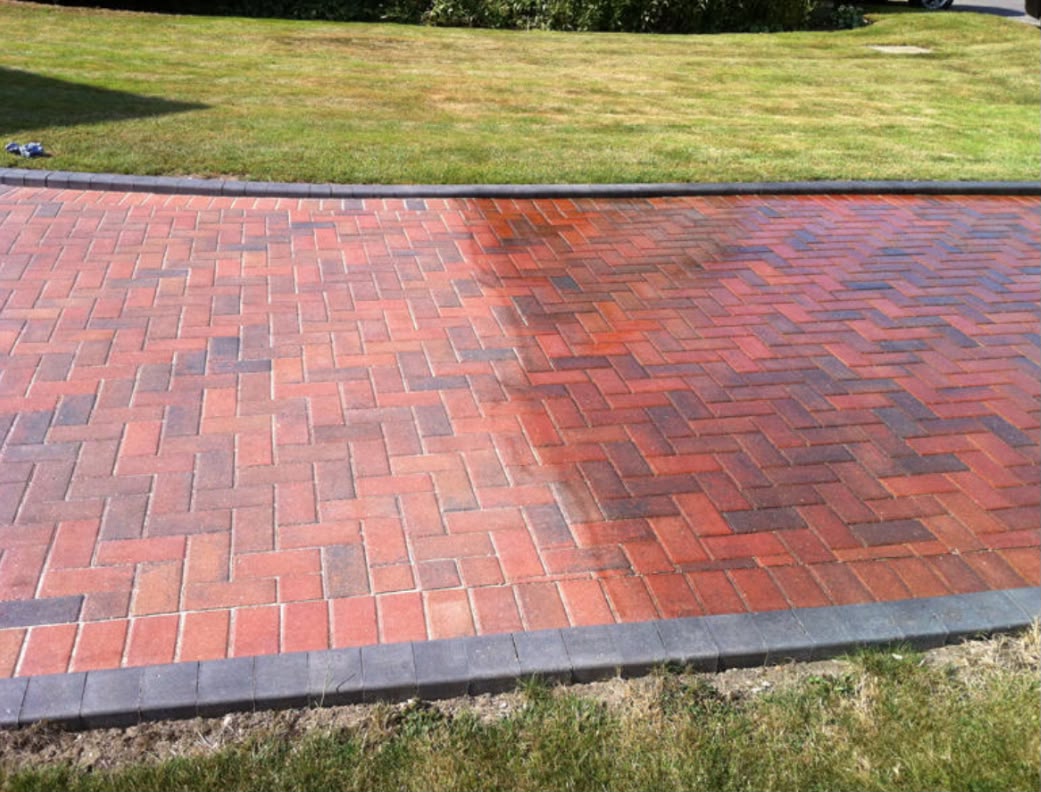 Faded red block paving driveway half restored with jet washing