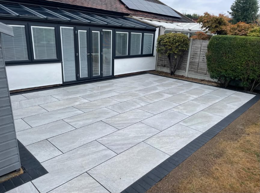 Grey porcelain patio with charcoal picture-frame border behind a conservatory